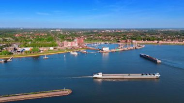 Güneşli bir günde uzun mavnalar huzurlu sularda hareket eder. Lelystad Limanı, Hollanda ve yemyeşil zemin üzerindeki şehir manzarası. Hava görünümü.