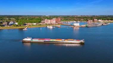 Mavna, güzel mavi deniz manzarasının yanındaki konteynırlarla dolu. Lelystad Limanı, Hollanda ve yeşil şehir manzarası. Hava görünümü.