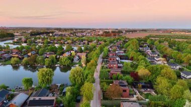 Deniz kıyısındaki köyün üzerinde uçuş. Gün batımında yemyeşil yemyeşil bir kırsal alan. Hava görüntüsü. Vinkeveen, Hollanda.