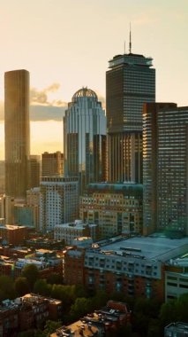 Boston, Massachusetts, ABD 'de güneş batıyor. Düşük katlı apartmanların üstündeki insansız hava aracı görüntüleri gökdelenlerden uzaklaşıyor. Dikey video