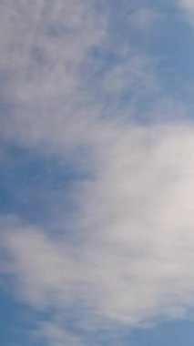 Mavi gökyüzü ve yukarıdan yayılan hafif tüy bulutları. Güneş ufukta süzülen küçük bulutları aydınlatıyor. Düşük açı. Zaman ayarlı. Dikey video