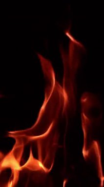 Karanlıkta dans eden şenlik ateşinin güzel alevleri. İnce alev dilleri yükseliyor. Kapatın. Dikey video