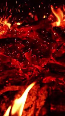 Kamp ateşinde odun yakmak. Bilinmeyen kişi kömürü hareket ettiriyor ve ışıldıyor. Kapatın. Arkaplanda karanlık var. Dikey video