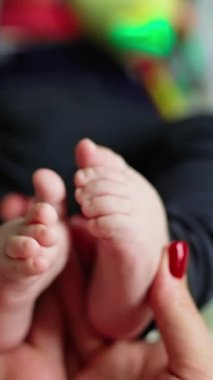 Minik bebek ayakları annenin ellerinde. Küçük bebeğin ayakları kadının ellerinde, yakın plan. Dikey video