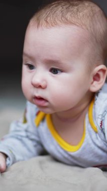 Yatakta yatan neşeli bir bebek. Sevimli mutlu küçük çocuk gülümsüyor. Dikey video