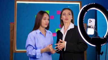 İki uzun saçlı esmer telefonun başında yüzük ışığıyla bekliyor. Kadınlar konuşur, tartışır, blog çekimlerine hazırlanır..