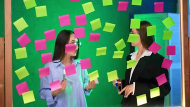 Cam levhanın arkasında etiketlerle kaplı gözlüklü kadınlar. Kadınlar iş meselelerine katılmıyor veya tartışıyorlar.