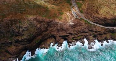 Bitki örtüsü zayıfken ulaşılmaz kayalar sersemletiyor. Kayalıklarda köpüklü su sıçrayan dalgalar. Üst görünüm.