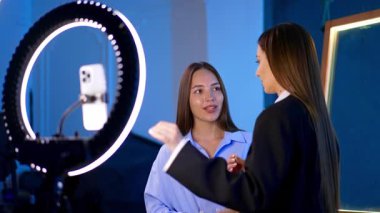 Geveze güzellik dersi. Stüdyo ortamında sohbet eden iki kadın, halka ışığı ve akıllı telefon ayarlı bir güzellik dersine hazırlanıyor..