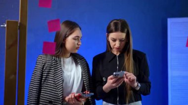 Toplantı sırasında fikirler hakkında tartışırız. İki kadın, parlak renklere sahip yaratıcı bir çalışma alanında akıllı bir telefona bakarken odaklanmış bir tartışma içindeler..