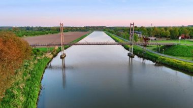 Hollanda 'nın sakin suları üzerinde köprü. Günbatımı, yemyeşil ve tarlalarla çevrili sakin bir kanalı kaplayan köprünün üzerinde sıcak bir ışıltı yayar..