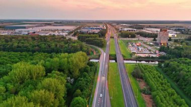 Hollanda otoyolunda gün batımı. Gün batımında Hollanda 'da bir otoyolun hava perspektifi yeşillik ve gelişmiş bölgeler sergilenmektedir..