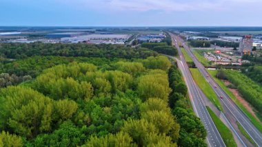 Yeşil ormanın yakınından hızla geçen arabalar var. Arka plandaki modern küçük kasabanın altyapısı. Hava görünümü.