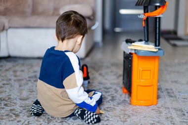 Çocuk oyuncak aletlerle oynuyor. Küçük bir çocuk, hayal gücüne odaklanmış, rahat bir oturma odasında oyuncak setiyle etkileşime girer..
