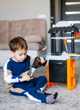 Oyuncak aletlerle oynayan bir çocuk. Küçük çocuk oyuncak matkabını kullanarak ev ortamında konsantrasyon ve yaratıcılık göstererek nesneleri birleştirir..