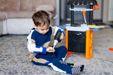 Çocuk evde sondaj oyuncağıyla oynuyor. Küçük çocuk rahat bir oturma odasında halının üzerinde oynarken oyuncak matkap kullanmaya odaklanmış..