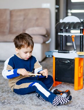 Çocuk oyuncak mutfağıyla oynuyor. Genç bir çocuk evde renkli bir oyuncak mutfağıyla meşgul oluyor, ahşap bir oyuncağa odaklanıyor ve oyun zamanının tadını çıkarıyor..