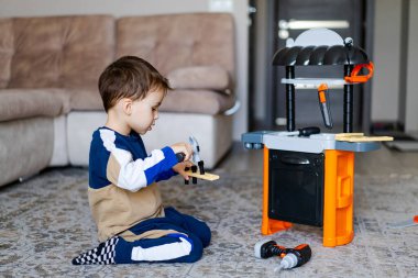 Çocuk oyuncakçıyla oyun oynuyor. Küçük bir çocuk halının üzerinde oturuyor, oyuncak mutfak takımıyla oynamaya odaklanmış, alet edevat ve aletleri yaratıcı bir şekilde kullanıyor..