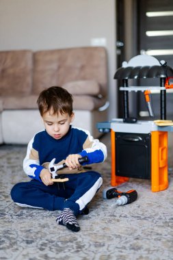 Yaratıcı oyundaki çocuk. Yerde oturan genç bir çocuk, oyuncak aletlerle, rahat bir odada oyun mutfağının yanına kurulmuş bir binaya odaklanmış..