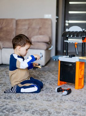 İçeride aletleri olan çocuk oyuncakları. Küçük bir çocuk oturma odasındaki halıya oturur, oyuncak aletlerle yaratıcı bir oyun oynar gibi mutfağa geçer..