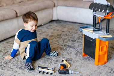 Çocuk oyuncak aletlerle oynuyor. Çocuk, oyuncak tezgahıyla yaratıcı oyunlardan ve rahat bir oturma odasında rahat bir halıda aletlerden hoşlanıyor..