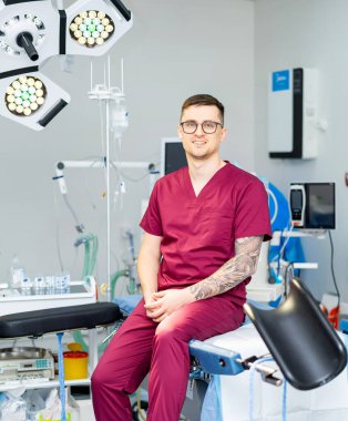 Ameliyathanede ameliyat cerrahı. Burgonya önlük giyen cerrahlar tıbbi ekipman ve ışıklarla çevrili modern bir ameliyathanede güvenle otururlar..