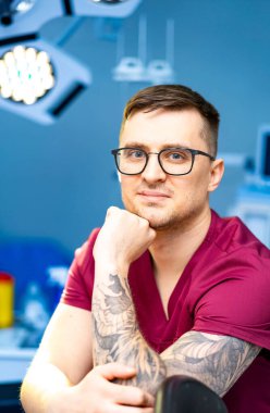 Klinikteki kendine güvenen doktor. Dövmeli bir erkek sağlık görevlisi klinikte oturup uzman hasta bakımı sağlamaya hazır..