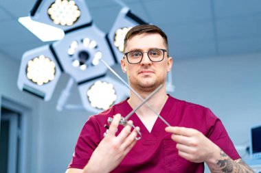 Cerrah aletleri gösteriyor. Önlüklü bir sağlık görevlisi, iyi aydınlatılmış bir tıbbi ortamda cerrahi aletler sergiliyor..