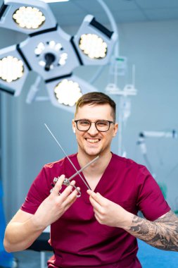 Cerrah modern ameliyathanede gülümsüyor. Ameliyat önlüklü bir cerrah iyi donanımlı bir ameliyathanede cerrahi aletlerle memnuniyetle poz verir..