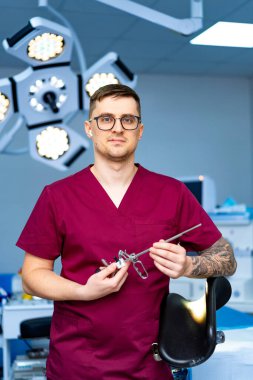 Cerrah ameliyata hazırlanıyor. Cerrah modern bir ameliyathanede elinde cerrahi aletlerle bekliyor ve yaklaşan prosedüre hazır..