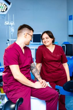 Klinikler: Sağlık hizmetleri ekip çalışması. Klinik bir ortamda bir prosedüre hazırlanırken iki sağlık personeli dostça bir konuşma yapıyor..