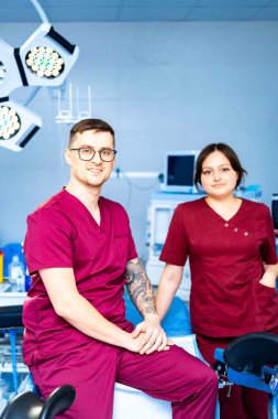 Dişçi kliniği profesyonelleri. İki dişçi uzmanı tıbbi ekipmanlarla dolu modern bir klinikte poz veriyor, takım çalışmalarını ve uzmanlıklarını sergiliyorlar..