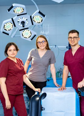 Cerrahi sağlık uzmanları. Üç sağlık uzmanı, gündüz vakti parlak bir cerrahi ameliyathanede güven içinde poz veriyorlar..