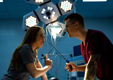 Doktorlar şakayla yarışıyor. İki tıp çalışanı gündüz vakti iyi donanımlı bir cerrahi odada birbirlerine makas ile meydan okuyorlar..