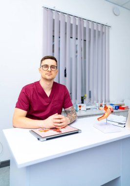 Muayene odasında doktor var. Bir tıp uzmanı danışma odasındaki bir masada oturmuş, tartışmayla meşgul. Modeller ve tablolar görünür..