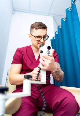 Doktor tıbbi cihazı kontrol ediyor. Önlüklü bir sağlık çalışanı, klinik ortamda odaklanma ve profesyonelliğe sahip tıbbi bir cihazı inceler..