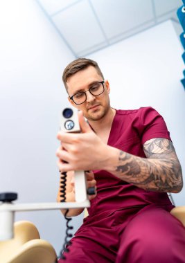 Dişçi ofiste ekipman hazırlıyor. Ameliyat önlüğü giymiş bir diş hekimi, modern bir klinikte çalışma saatleri içinde aletleri inceler ve ayarlar..