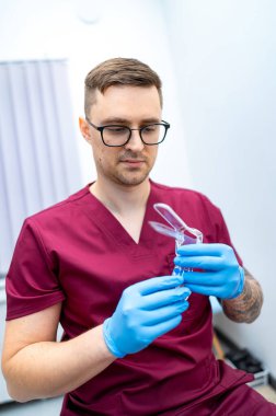 Klinikte dişçi aletleri hazırlıyor. Kestane rengi bir uzman, klinikte mavi eldiven giyerken aletleri ustalıkla temizler..