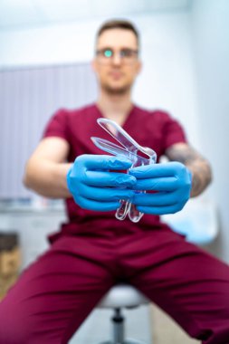 Doktor işleme hazır. Bir tıp uzmanı klinikte oturur, mavi eldivenler giyer ve ameliyat aletlerini tutar, çalışmaya hazırdır..