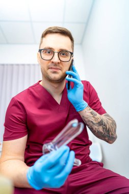 Doktor hastaya yardım eder. Doktor önlüğü uzmanı elinde tıbbi ekipman varken telefonda konuşuyor. Hastaya yardım etmeye hazır..