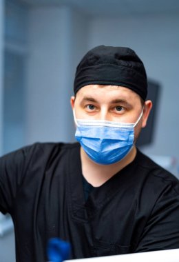 Uzmanlardan sağlık desteği. Ameliyat önlüğü ve maske takan bir sağlık görevlisi, klinik bir ortamda hastanın bakımını sağlama görevine odaklanır..