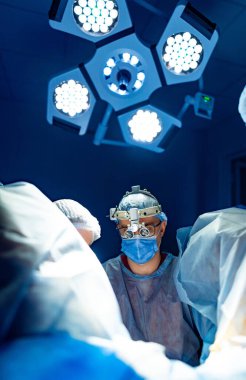 Hassas ameliyatta bir cerrah. Yetenekli bir cerrah parlak ışıklar altında gelişmiş aletler kullanırken bir ekip de önemli bir tıbbi operasyona odaklanıyor..