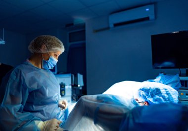 Cerrah hassas bir ameliyat yapar. Bir cerrah ve asistan, iyi aydınlatılmış bir ameliyathanede hastanın güvenliğini sağlamak için cerrahi bir operasyona odaklanırlar..