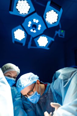 Modern bir ameliyathanede cerrahlar. Cerrahi ekip, steril bir ortamda parlak ışıklar altında titizlikle çalışarak takım çalışmalarını ön plana çıkarıyor..