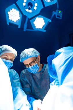 Ameliyathanede ekip çalışması. Tıp uzmanları steril bir ortamda, parlak ışıklar altında kritik bir prosedüre odaklanarak birlikte çalışırlar..