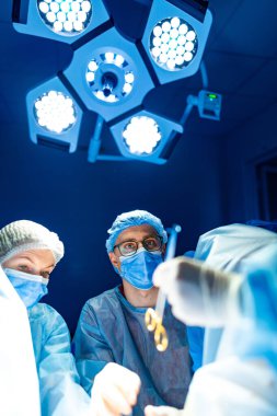 Hastanedeki cerrahi ekibi. Cerrahlar ve hemşireler, parlak ışıklar altında hastanın güvenliğini ve bakımını sağlamak için cerrahi prosedürlere dikkatle odaklanıyorlar..