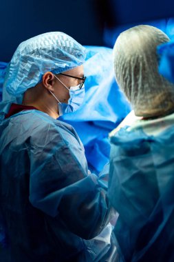 Tıbbi ekip tarafından ameliyat. Koruyucu giysili cerrahlar ameliyathanede iş birliği yaparlar, ameliyat sırasında hastalara öncelik verirler..