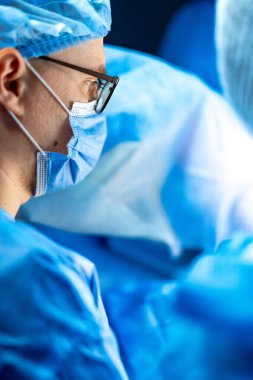 Cerrahi sağlık personeli. Mavi önlüklü cerrah steril aletleri ve tıbbi personeli olan bir operasyon üzerinde dikkatle çalışıyor..