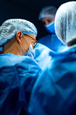 Cerrahlar hassas bir ameliyat yapıyor. Cerrahi giyimli tıp uzmanları, bir ameliyathanede karmaşık bir operasyon yaparken dikkatle odaklanırlar..
