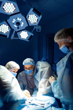 Steril operasyonda cerrahi ekip. Cerrahlar ve hemşireler bir ameliyathanede parlak ve odaklanmış ışıklar altında cerrahi bir prosedürde işbirliği yaparlar..
